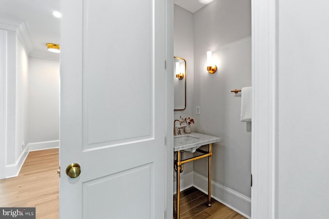 interior space featuring wood finished floors, crown molding, baseboards, and a sink