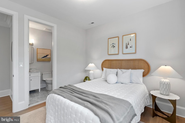 bedroom with ensuite bath, wood finished floors, visible vents, and baseboards