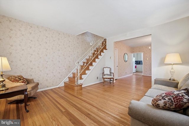 living area featuring wallpapered walls, wood-type flooring, baseboards, and stairway