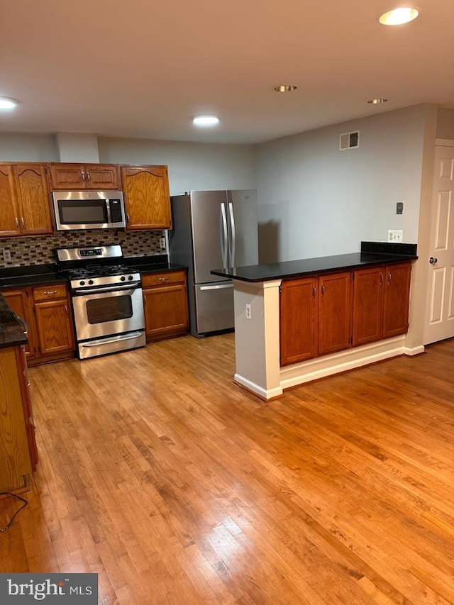 kitchen featuring stainless steel appliances, light wood-style flooring, dark countertops, backsplash, and brown cabinetry