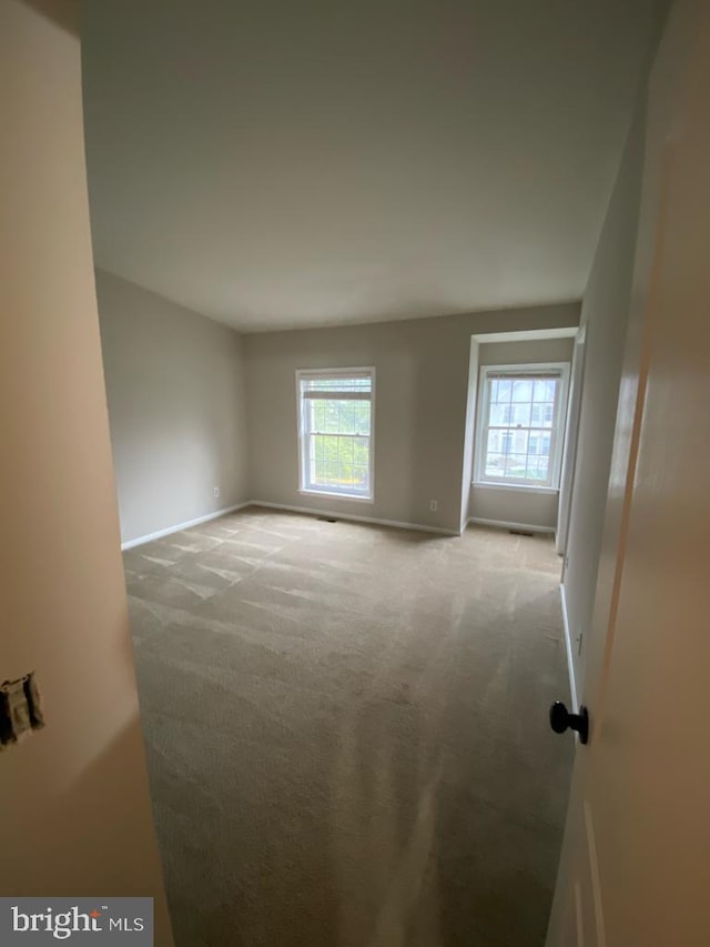 spare room featuring light carpet, baseboards, and healthy amount of natural light