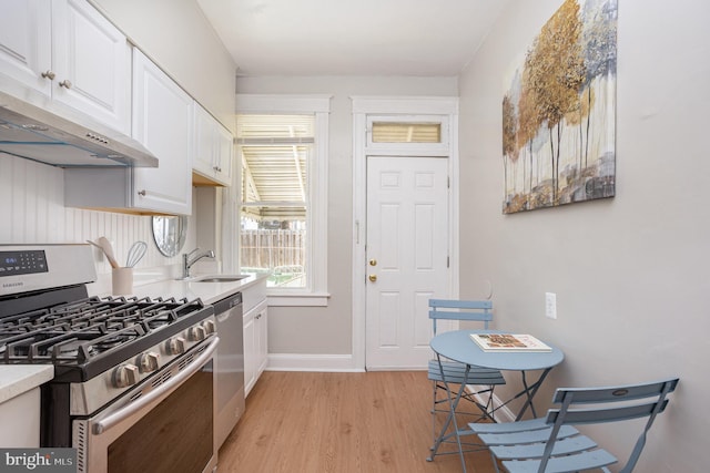 kitchen with appliances with stainless steel finishes, a sink, light wood-style floors, white cabinets, and under cabinet range hood