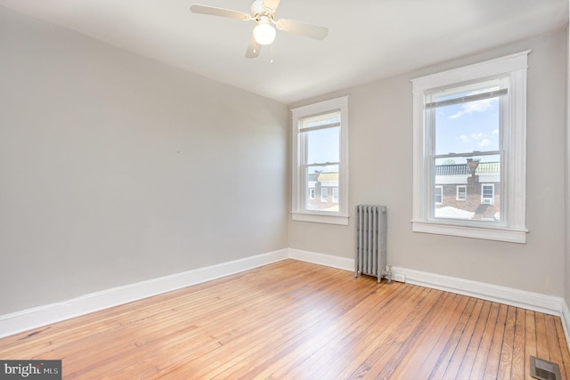 empty room featuring radiator heating unit, light wood-type flooring, baseboards, and a ceiling fan