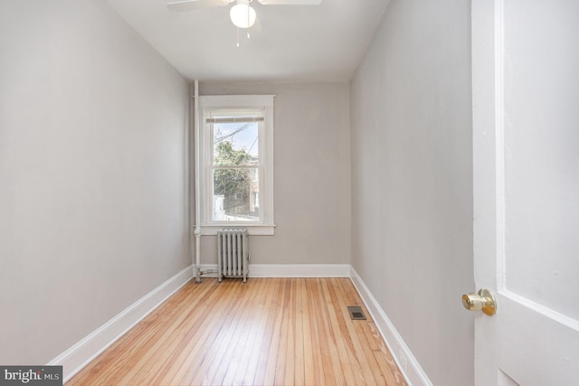 empty room featuring radiator, light wood-type flooring, a ceiling fan, and baseboards