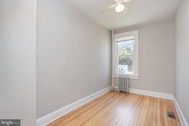 unfurnished room featuring radiator heating unit, light wood-style flooring, baseboards, and ceiling fan