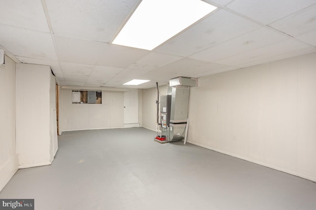 finished basement with a drop ceiling, electric panel, and heating unit