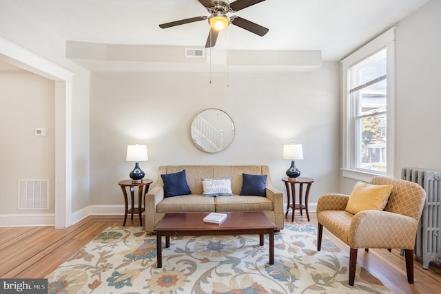 living room featuring wood finished floors, baseboards, radiator, and ceiling fan