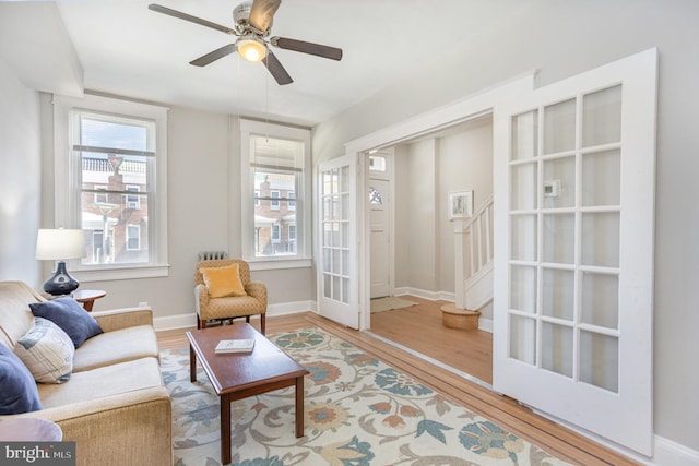 living room with wood finished floors, a ceiling fan, baseboards, and stairway