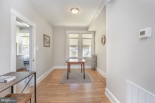 corridor featuring light wood-style flooring, radiator heating unit, and baseboards