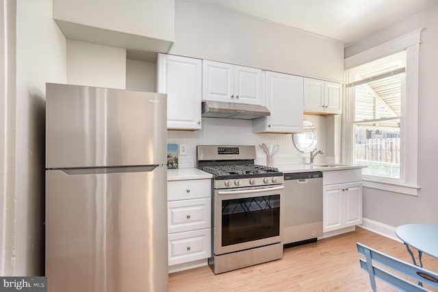 kitchen with stainless steel appliances, under cabinet range hood, a sink, and white cabinetry