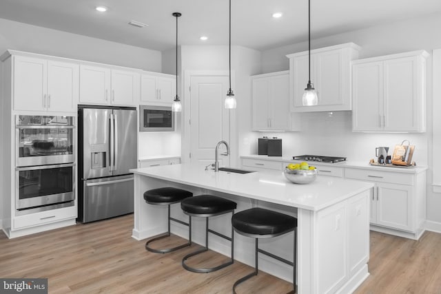 kitchen featuring white cabinets, light countertops, a sink, stainless steel appliances, and light wood finished floors