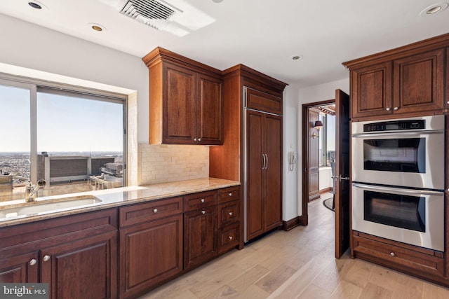 kitchen with a sink, visible vents, double oven, and light stone counters