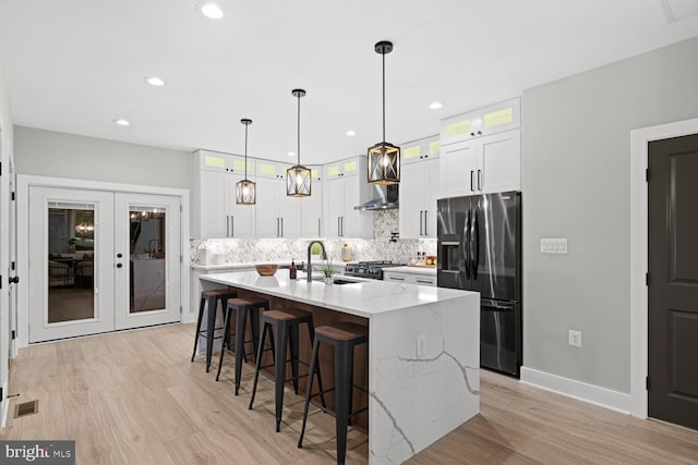 kitchen featuring stainless steel fridge with ice dispenser, wall chimney exhaust hood, a sink, light wood-style floors, and backsplash