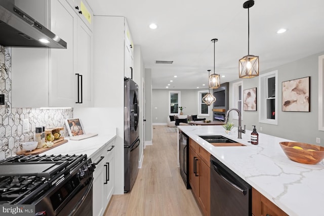 kitchen featuring stainless steel dishwasher, ventilation hood, a sink, freestanding refrigerator, and light wood finished floors