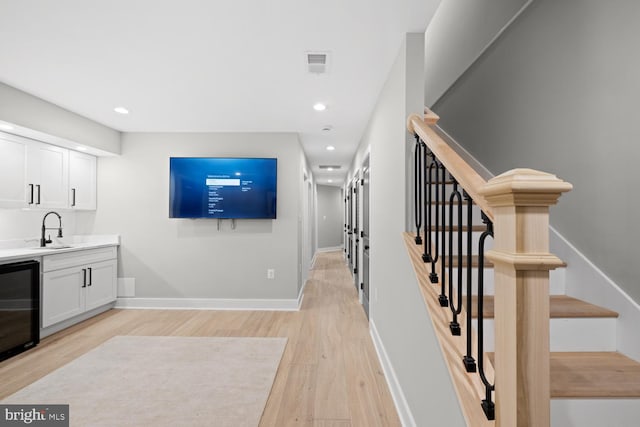 staircase featuring wood finished floors, beverage cooler, recessed lighting, baseboards, and bar with sink