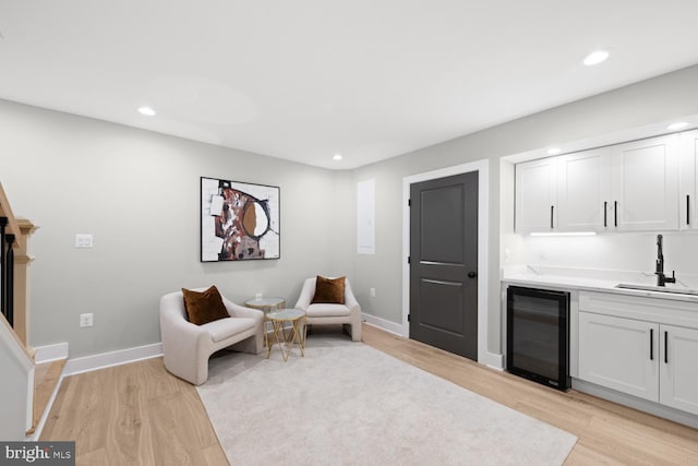 sitting room with beverage cooler, light wood-type flooring, bar with sink, recessed lighting, and baseboards