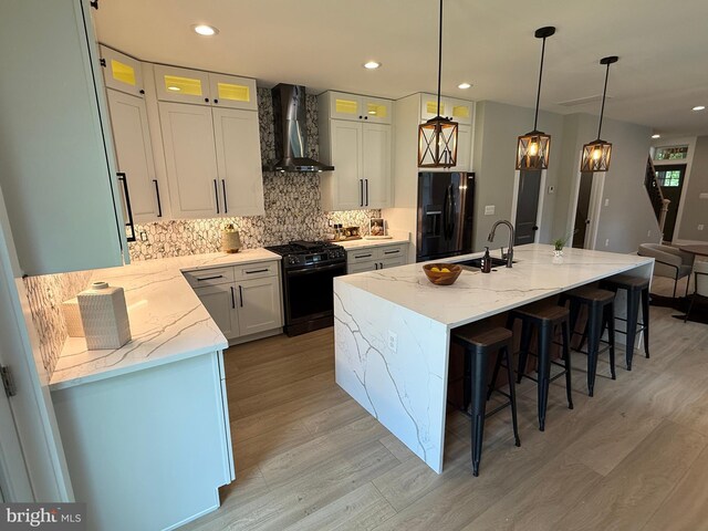 kitchen featuring black appliances, wall chimney exhaust hood, a sink, light wood-style flooring, and backsplash