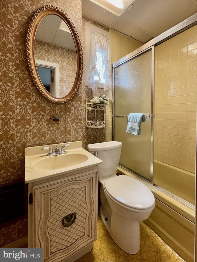 full bathroom featuring toilet, vanity, bath / shower combo with glass door, and wallpapered walls