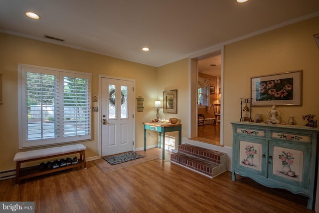 foyer entrance with crown molding, baseboards, wood finished floors, and visible vents