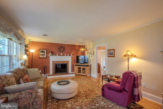 living area featuring baseboards, ornamental molding, a glass covered fireplace, and wood finished floors