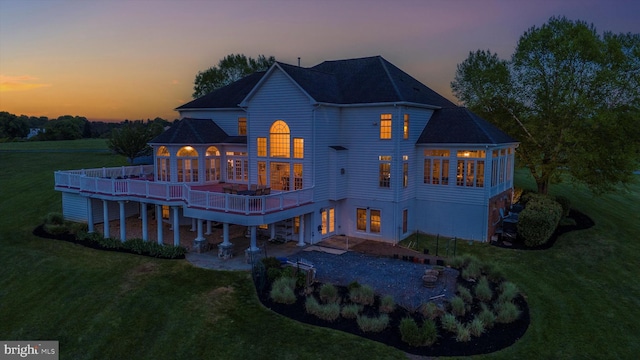 back of house at dusk with a lawn, a deck, a sunroom, and a patio area