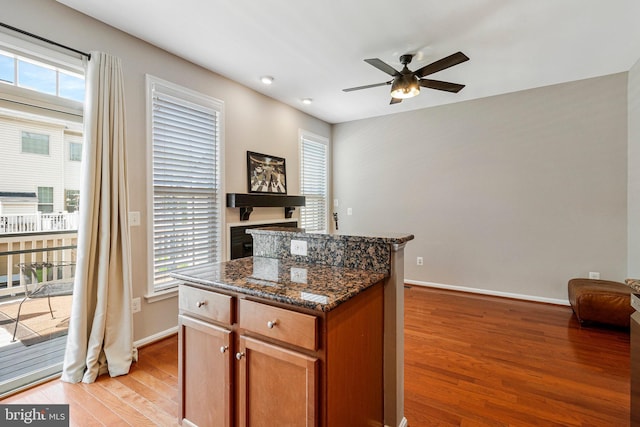kitchen featuring a ceiling fan, a center island, baseboards, light wood-style floors, and a wealth of natural light