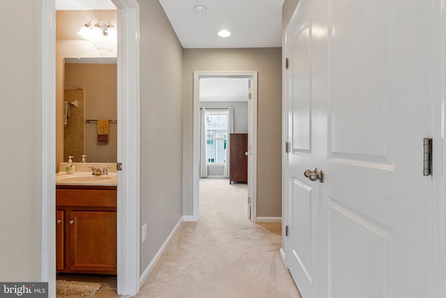 corridor featuring light colored carpet, a sink, and baseboards