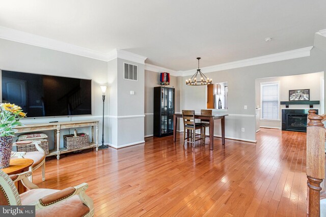 living room featuring visible vents, crown molding, a glass covered fireplace, a chandelier, and light wood-style flooring