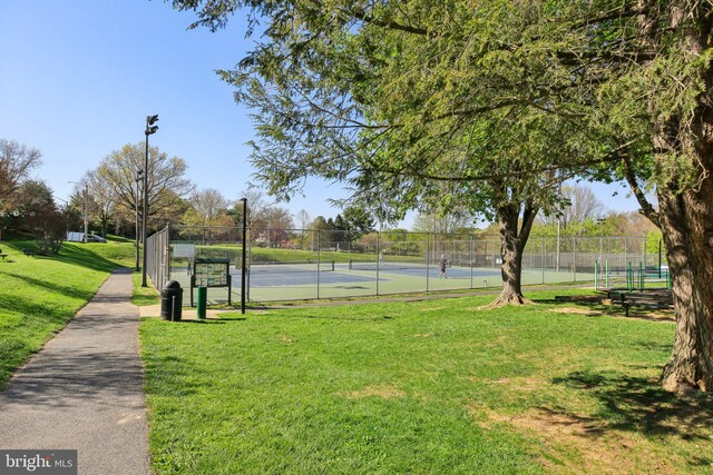 view of property's community featuring a tennis court, a lawn, and fence