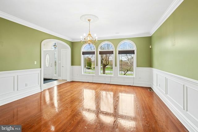 spare room featuring a notable chandelier, crown molding, a wainscoted wall, arched walkways, and wood finished floors