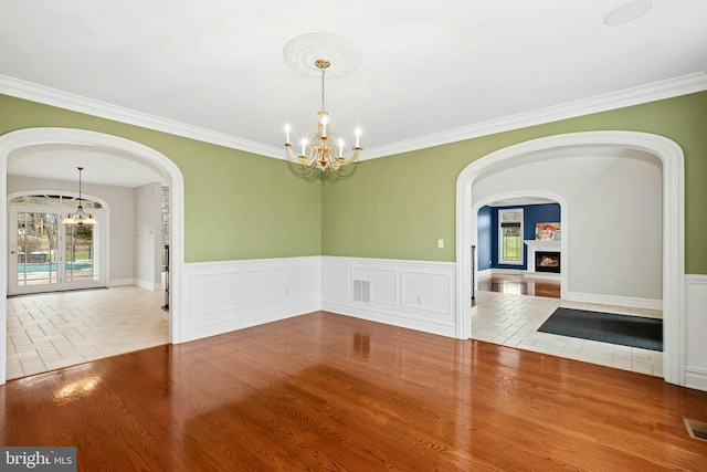 spare room featuring arched walkways, wood finished floors, a notable chandelier, and visible vents