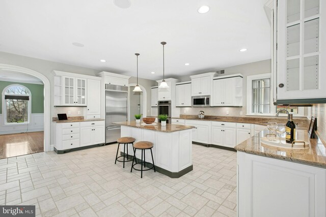 kitchen featuring open shelves, recessed lighting, appliances with stainless steel finishes, and a kitchen bar