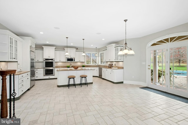 kitchen with a kitchen breakfast bar, recessed lighting, a center island, white cabinetry, and appliances with stainless steel finishes