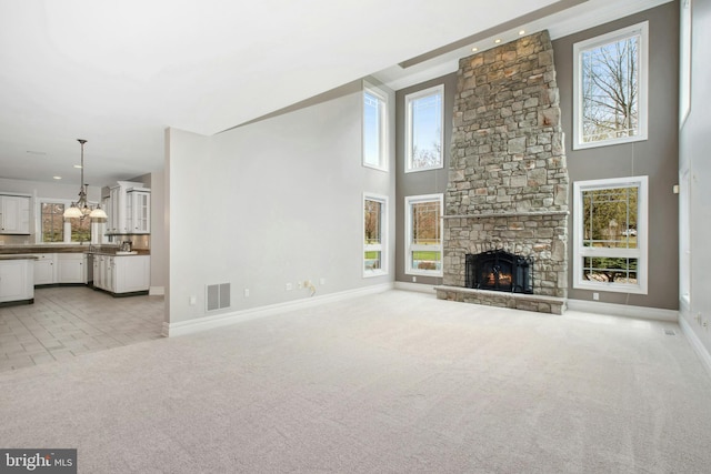 unfurnished living room with visible vents, baseboards, a stone fireplace, a towering ceiling, and light colored carpet