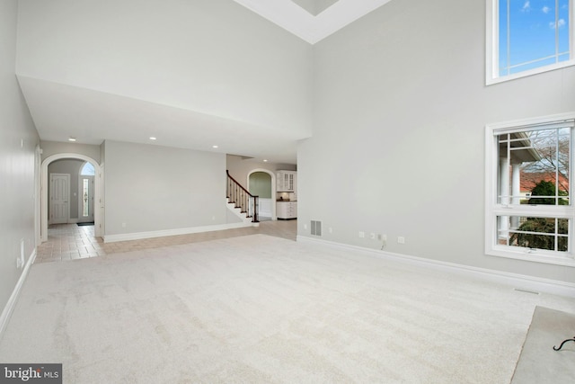 unfurnished living room featuring light carpet, arched walkways, a towering ceiling, and baseboards
