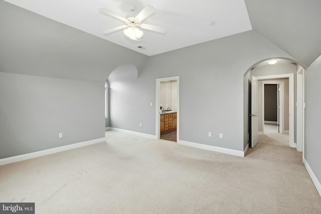 unfurnished bedroom with arched walkways, light colored carpet, visible vents, lofted ceiling, and baseboards