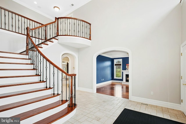 entryway with baseboards, arched walkways, a high ceiling, ornamental molding, and a lit fireplace