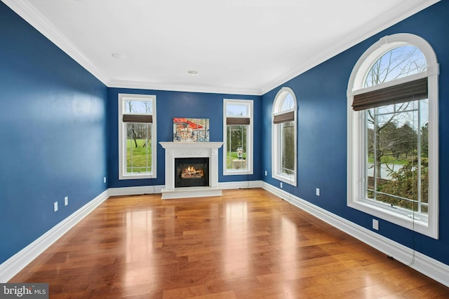 unfurnished living room featuring crown molding, wood finished floors, baseboards, and a glass covered fireplace