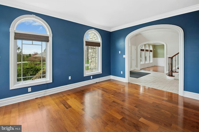 unfurnished room with arched walkways, stairway, baseboards, and hardwood / wood-style floors