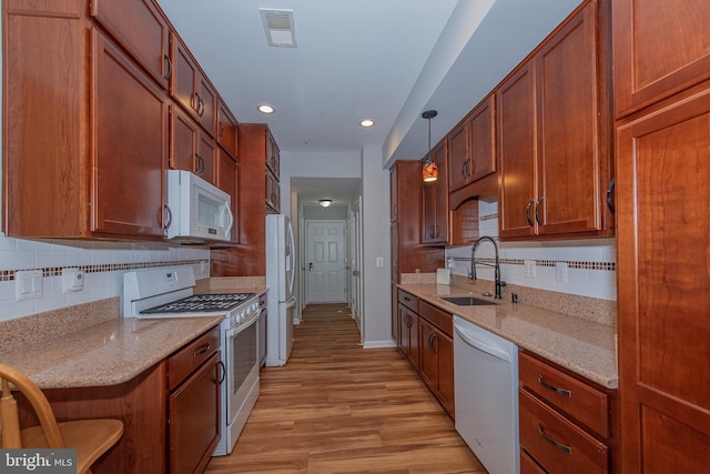 kitchen with a sink, white appliances, light wood finished floors, backsplash, and visible vents