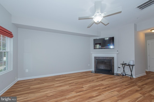 unfurnished living room featuring light wood finished floors, a high end fireplace, visible vents, baseboards, and ceiling fan