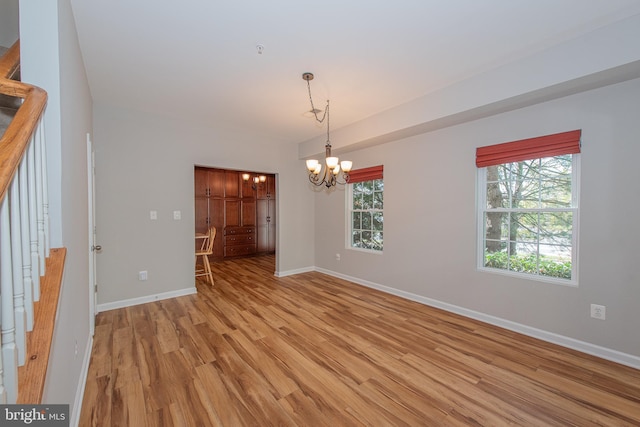 spare room featuring light wood-type flooring, baseboards, a notable chandelier, and stairs