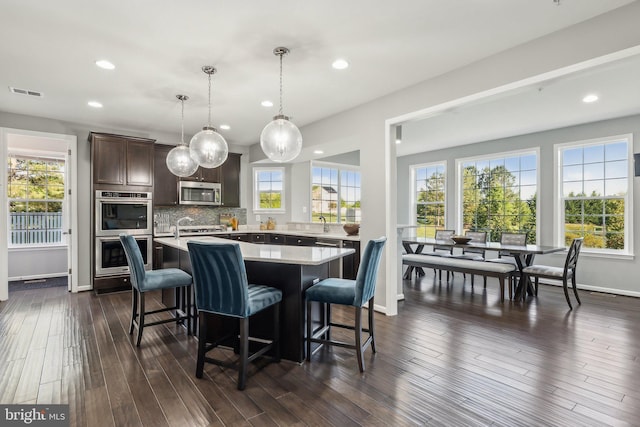 kitchen featuring visible vents, a kitchen island, dark brown cabinets, light countertops, and appliances with stainless steel finishes