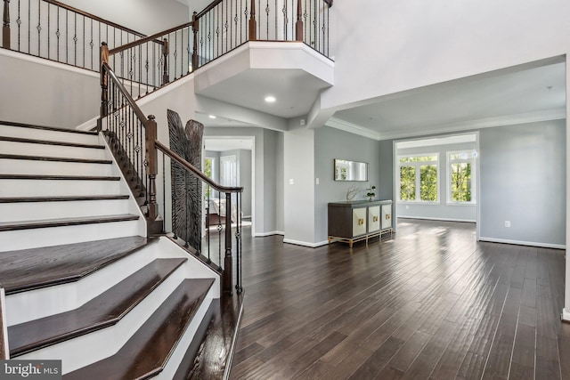 foyer entrance with baseboards, crown molding, wood finished floors, and stairway