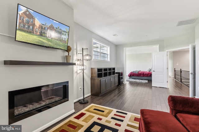 living room with visible vents, dark wood finished floors, a glass covered fireplace, and baseboards