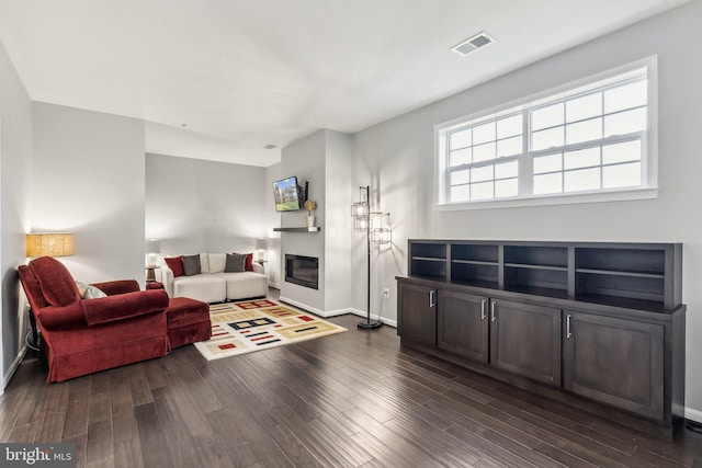 living area with a glass covered fireplace, baseboards, dark wood-style floors, and visible vents