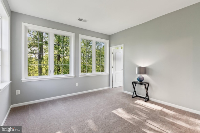 empty room featuring carpet floors, baseboards, visible vents, and a healthy amount of sunlight