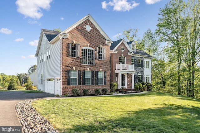 colonial home with a front yard, brick siding, a balcony, aphalt driveway, and an attached garage