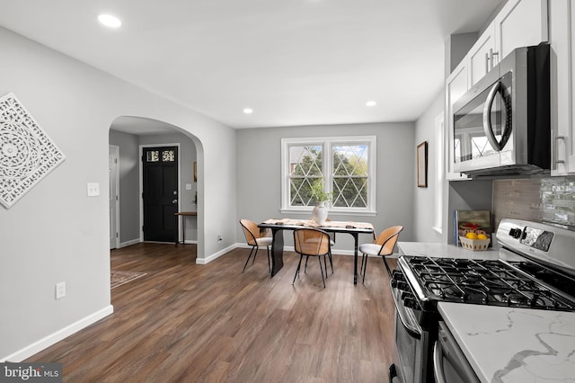 4319 Valley View Ave, Baltimore, MD 21206 - kitchen featuring wood finished floors, arched walkways, light stone countertops, appliances with stainless steel finishes, and white cabinetry