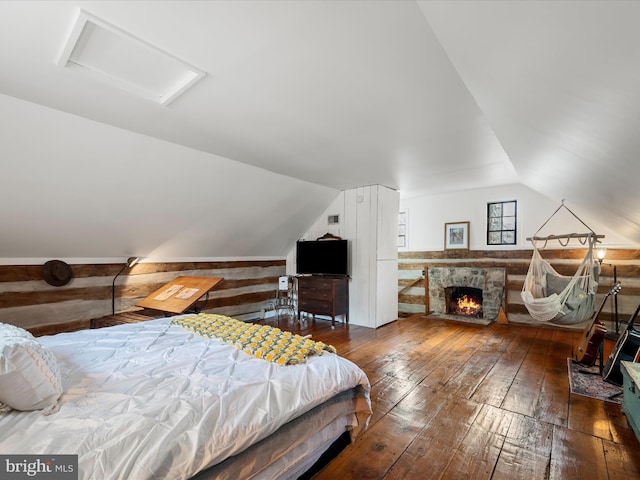 bedroom with hardwood / wood-style floors, lofted ceiling, wooden walls, a fireplace, and attic access